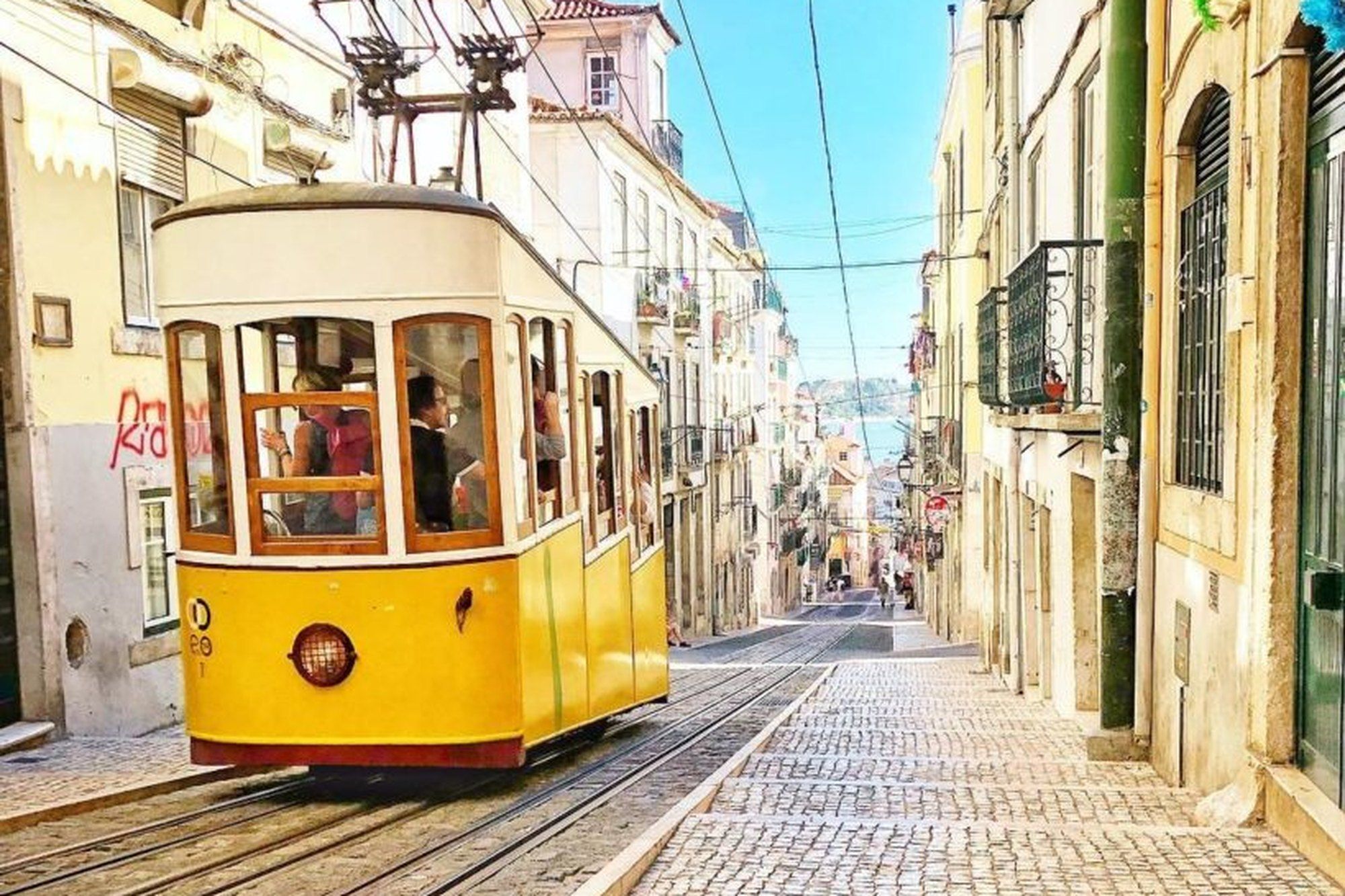 The yellow Bica funicular climbing a steep Lisbon street between pastel houses at golden hour