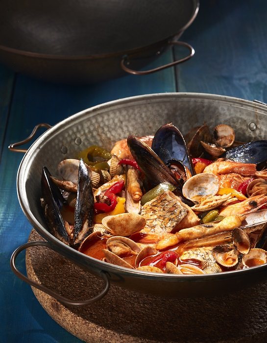 Une cataplana de cuivre ouverte à table dans un nuage de vapeur
