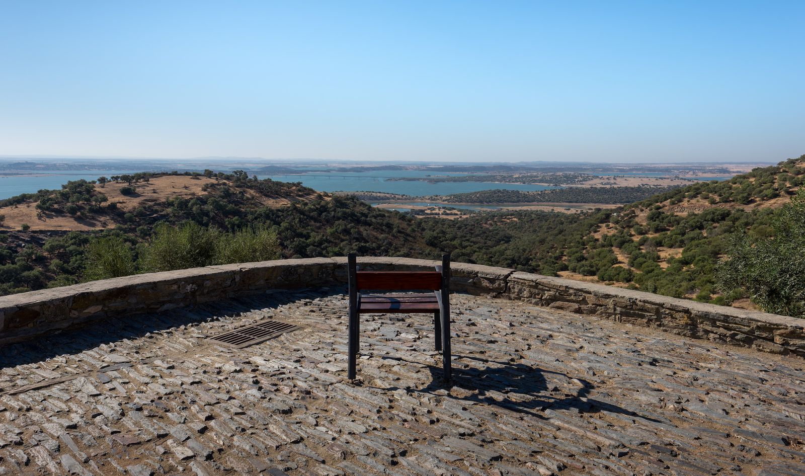 A single chair on the stone terrace of Monsaraz Castle, facing the islands and blue waters of the Alqueva reservoir in the Alentejo